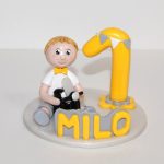 Figurine anniversaire 1 an de Milo, jaune et gris, tenant un vespa dans les mains.