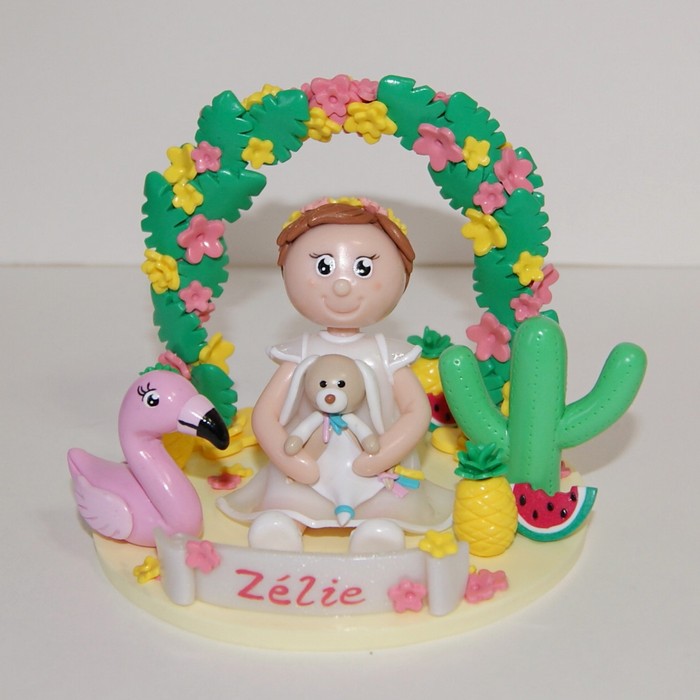 Figurine baptême, petite fille tenant son doudou, sur le thème tropical, avec flamant rose, cactus, ananas et pastèque