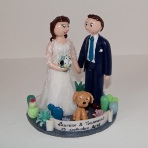 couple en tenue de mariage, avec leur caniche, sur socle recouvert de cactus et plantes grasses